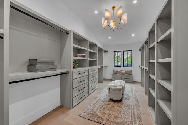walk in closet with lofted ceiling, light wood-style floors, and a notable chandelier