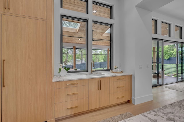 entryway featuring baseboards, a skylight, light wood finished floors, and a sink