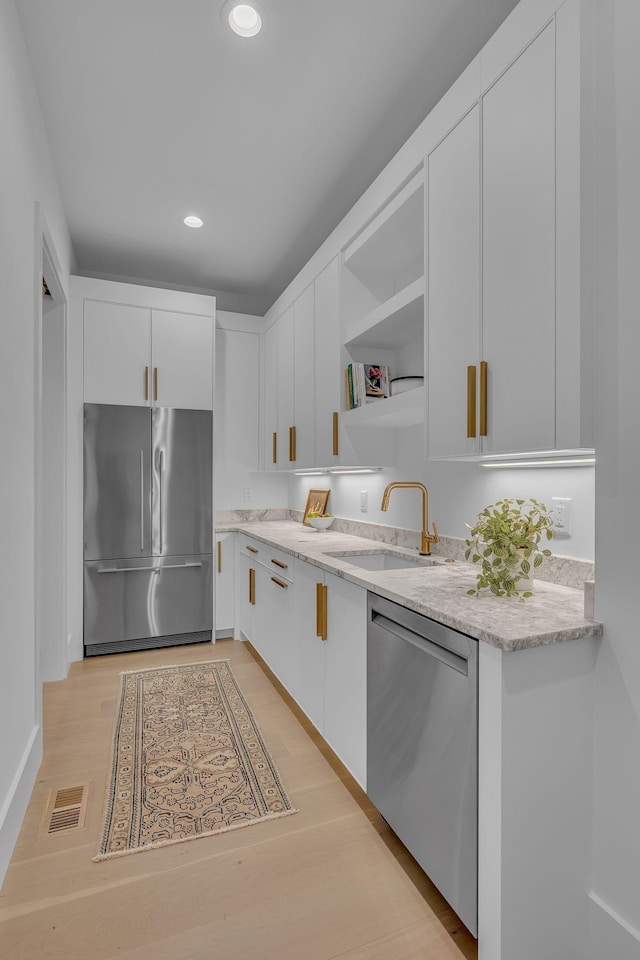 kitchen with white cabinets, light stone counters, appliances with stainless steel finishes, and a sink