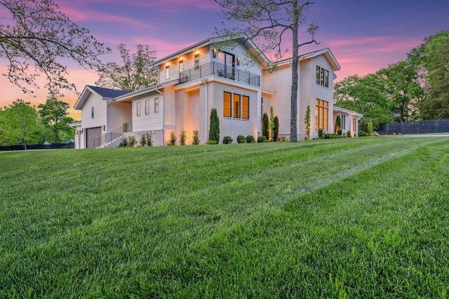 property exterior at dusk with stucco siding, a yard, fence, a garage, and a balcony