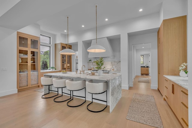 kitchen with light wood finished floors, light stone countertops, modern cabinets, recessed lighting, and a kitchen island with sink