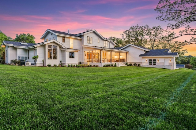 back of property at dusk featuring solar panels, a sunroom, and a lawn