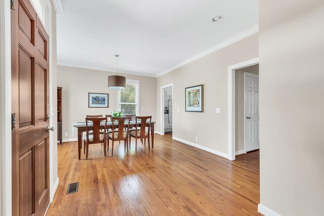 dining space featuring visible vents, crown molding, light wood-style flooring, and baseboards