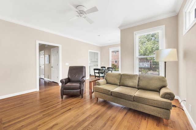 living room with light wood-type flooring, ceiling fan, baseboards, and crown molding