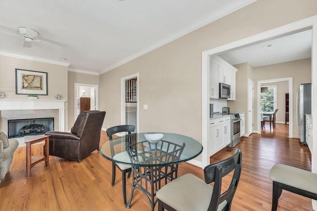 dining room featuring baseboards, ceiling fan, a premium fireplace, crown molding, and light wood-style floors