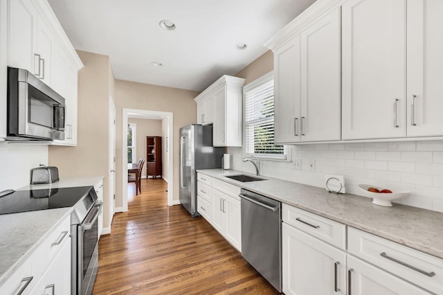 kitchen featuring white cabinets, decorative backsplash, wood finished floors, stainless steel appliances, and a sink