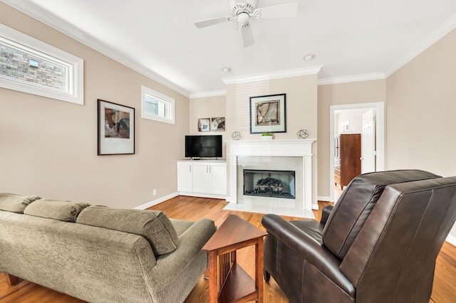 living area with baseboards, a ceiling fan, wood finished floors, crown molding, and a fireplace