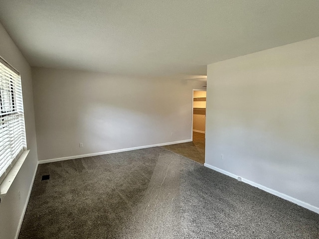 empty room with baseboards, visible vents, dark carpet, and a textured ceiling