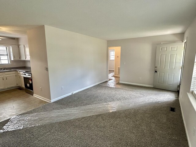 empty room with baseboards, a sink, visible vents, and light colored carpet