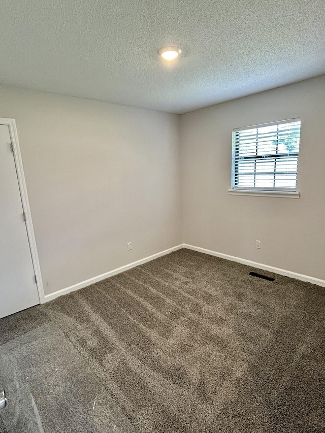 unfurnished room with a textured ceiling, dark colored carpet, visible vents, and baseboards