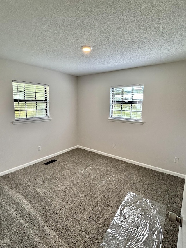 unfurnished room featuring a wealth of natural light, carpet flooring, visible vents, and baseboards