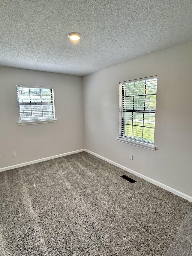 spare room with a healthy amount of sunlight, visible vents, baseboards, and carpet flooring