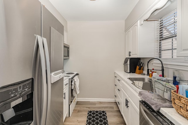 kitchen with appliances with stainless steel finishes, a sink, light wood-style flooring, and white cabinetry