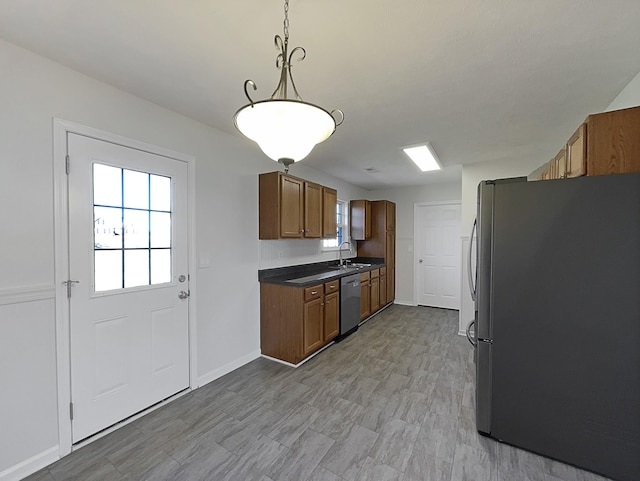 kitchen with plenty of natural light, dark countertops, appliances with stainless steel finishes, brown cabinets, and a sink