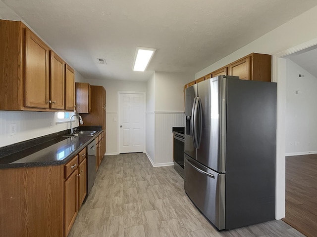 kitchen featuring brown cabinets, stainless steel appliances, visible vents, wainscoting, and a sink