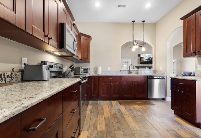 kitchen with hanging light fixtures, light wood-style floors, light stone counters, and stainless steel appliances