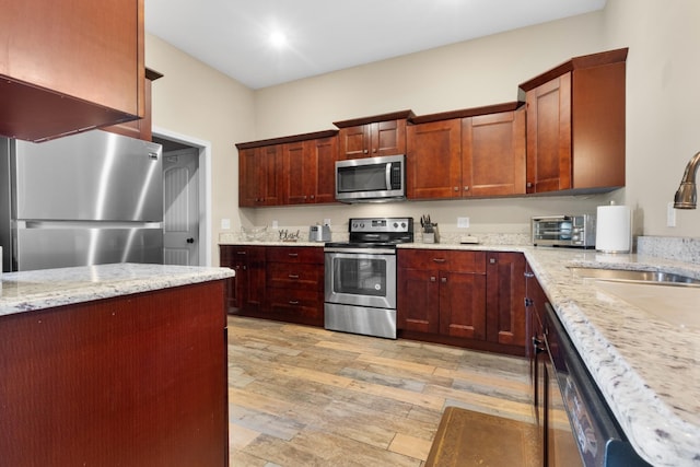 kitchen featuring a toaster, a sink, appliances with stainless steel finishes, light stone countertops, and light wood finished floors