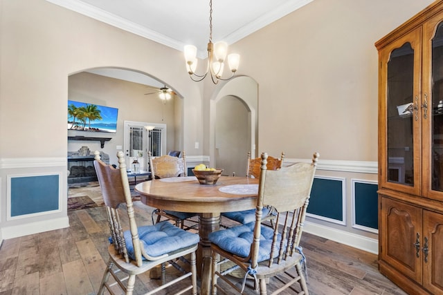 dining space with crown molding, a fireplace, arched walkways, and wood finished floors