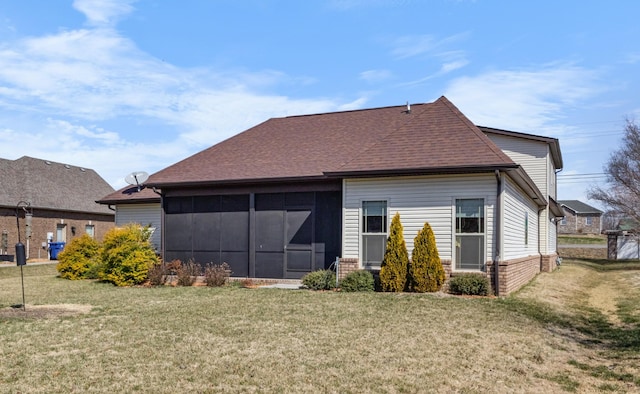 back of house featuring a sunroom, roof with shingles, brick siding, and a yard