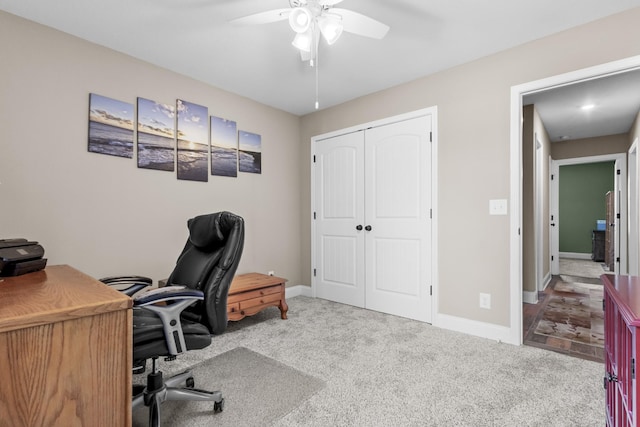 carpeted office space featuring ceiling fan and baseboards