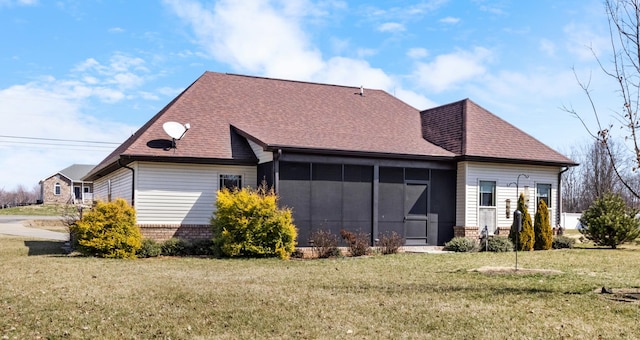 rear view of house with a sunroom, brick siding, a lawn, and roof with shingles