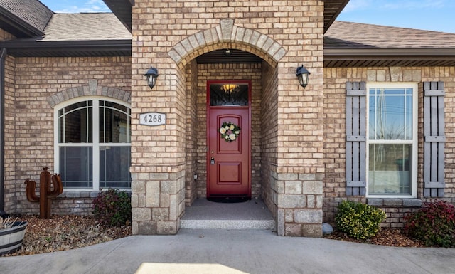 entrance to property featuring stone siding, roof with shingles, and brick siding