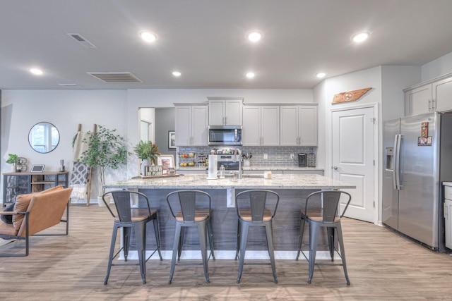 kitchen with light stone counters, a breakfast bar area, visible vents, appliances with stainless steel finishes, and a kitchen island with sink