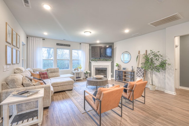 living room featuring light wood-type flooring, a fireplace, and visible vents