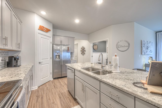 kitchen featuring gray cabinetry, stainless steel appliances, a sink, decorative backsplash, and light wood finished floors