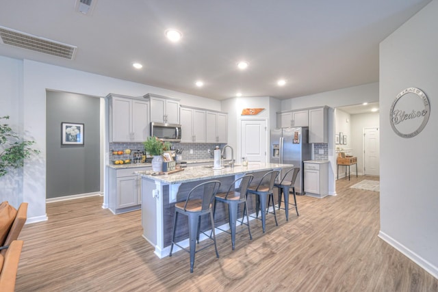 kitchen with stainless steel appliances, a breakfast bar, visible vents, and a center island with sink