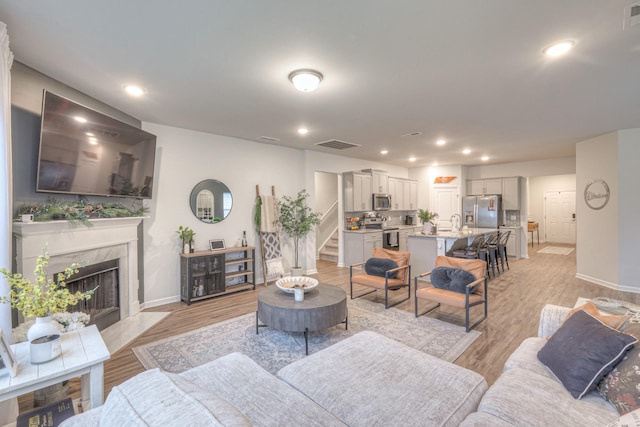 living area with visible vents, light wood finished floors, stairway, and a high end fireplace