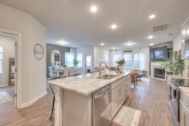 kitchen featuring visible vents, a fireplace with flush hearth, appliances with stainless steel finishes, open floor plan, and a sink