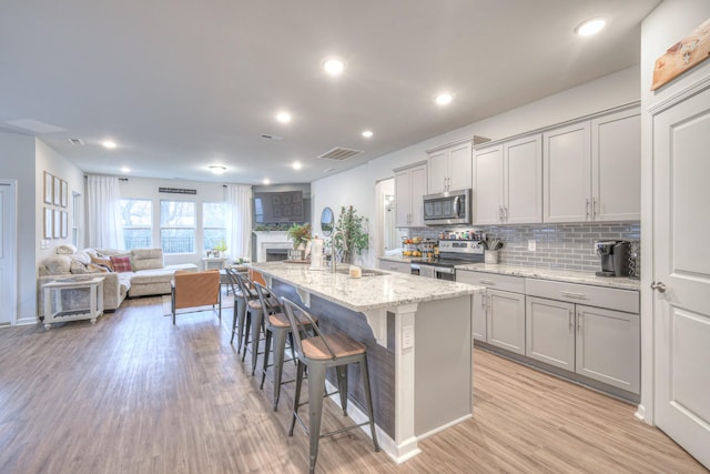 kitchen with a breakfast bar, light wood finished floors, stainless steel appliances, gray cabinets, and visible vents