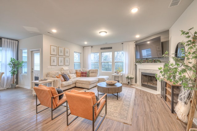 living area with a high end fireplace, visible vents, light wood finished floors, and recessed lighting