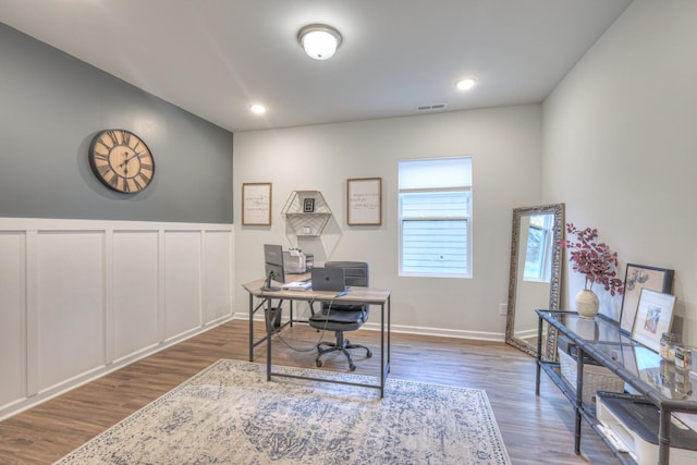 office area with wainscoting, visible vents, a decorative wall, and wood finished floors