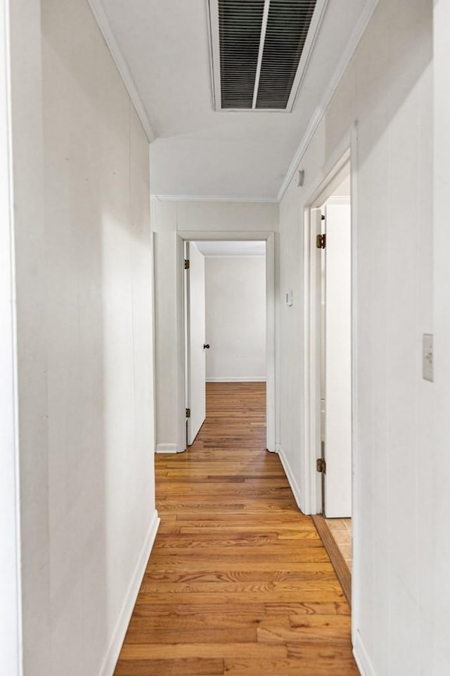 corridor featuring light wood finished floors, baseboards, visible vents, and crown molding