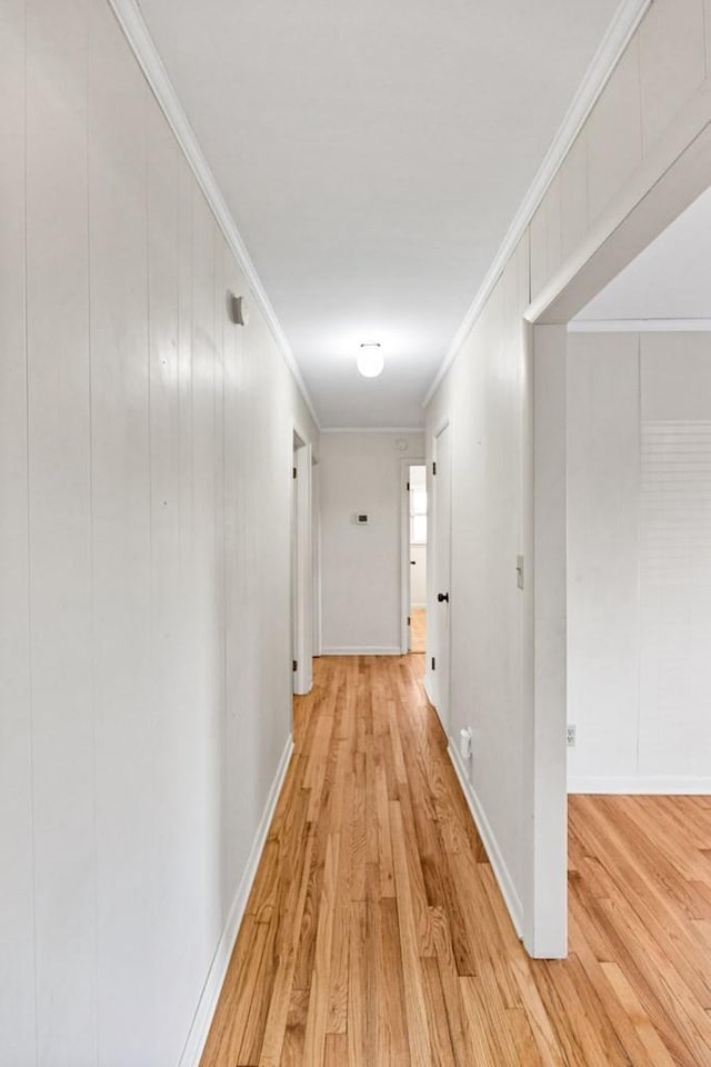 corridor featuring light wood-style flooring, ornamental molding, and baseboards