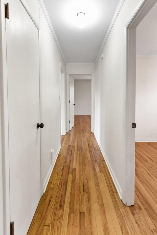 hall featuring light wood finished floors, baseboards, and ornamental molding