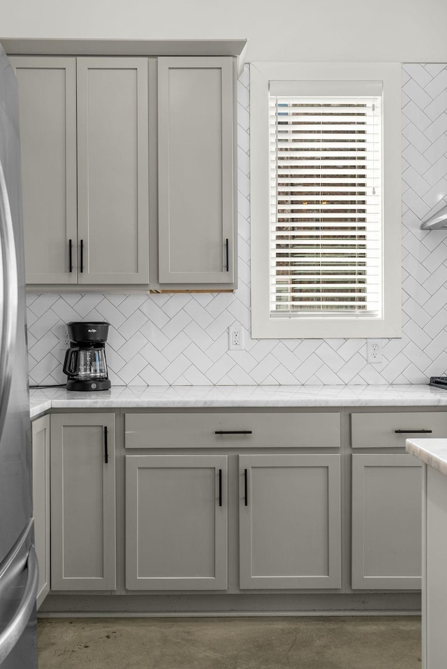 room details featuring light stone counters, tasteful backsplash, gray cabinets, and freestanding refrigerator