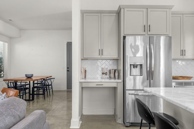 kitchen with stainless steel refrigerator with ice dispenser, tasteful backsplash, finished concrete floors, light stone countertops, and baseboards