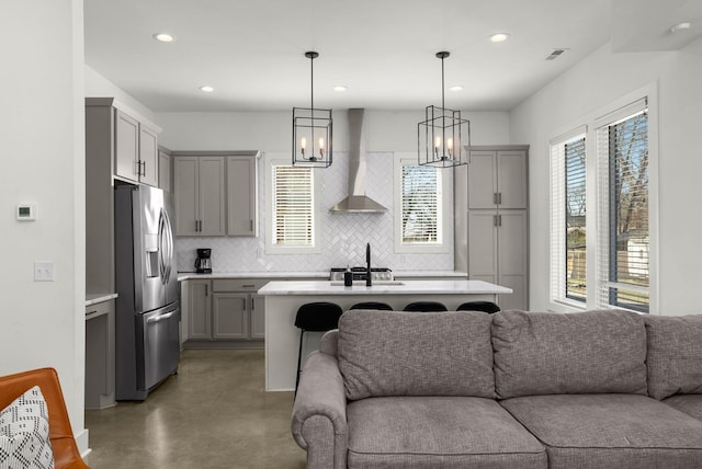 kitchen featuring wall chimney range hood, open floor plan, stainless steel refrigerator with ice dispenser, and gray cabinetry