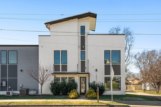 view of front facade with brick siding, fence, and central air condition unit