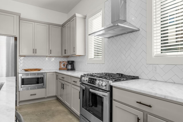 kitchen featuring concrete flooring, light stone counters, appliances with stainless steel finishes, wall chimney range hood, and tasteful backsplash