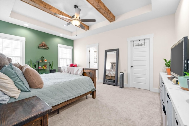 bedroom featuring multiple windows, a raised ceiling, beam ceiling, and light colored carpet