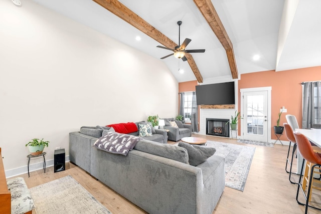 living room featuring light wood finished floors, baseboards, a ceiling fan, vaulted ceiling with beams, and a fireplace