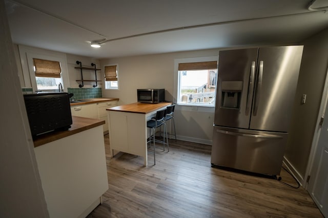 kitchen featuring tasteful backsplash, butcher block counters, appliances with stainless steel finishes, white cabinets, and wood finished floors