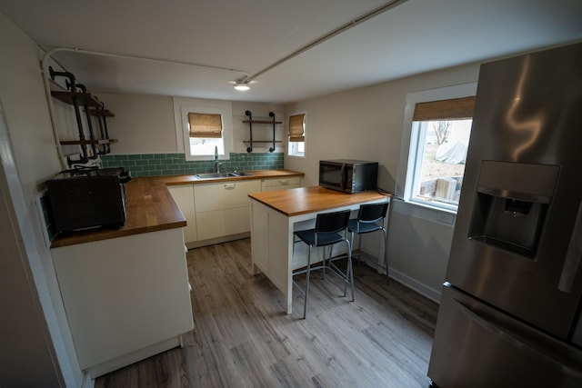 kitchen with black microwave, butcher block countertops, a sink, stainless steel refrigerator with ice dispenser, and backsplash