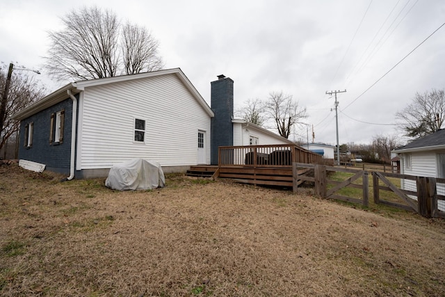 back of property with a deck, a chimney, and fence