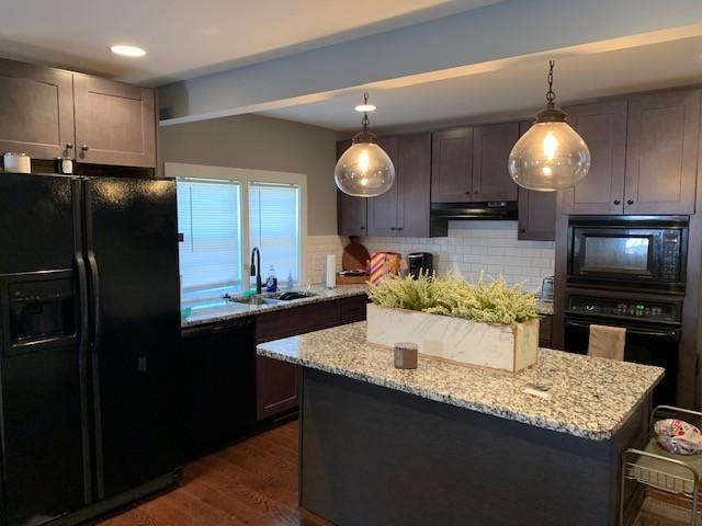 kitchen with a center island, light stone countertops, under cabinet range hood, black appliances, and a sink