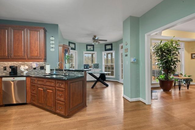 kitchen with decorative backsplash, a peninsula, light wood-type flooring, stainless steel dishwasher, and a sink